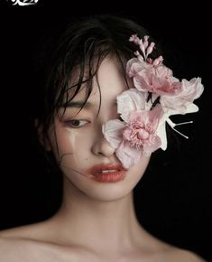 a woman with flowers in her hair and makeup is posing for the camera, she has one eye closed