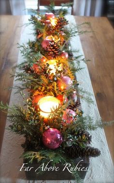 a long table is decorated with pine cones and christmas decorations, candles and evergreen branches