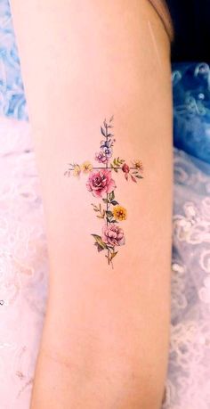 a cross tattoo with flowers on the side of the leg and behind it is an image of a woman's legs