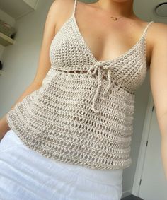 a woman is wearing a crocheted tank top and white skirt with her hands in her pockets