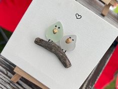 two birds sitting on top of a piece of wood next to a white board with hearts