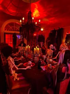 a group of people in skeleton costumes sitting around a table with food and candles on it