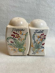 two salt and pepper shakers with flowers painted on the sides, one is white