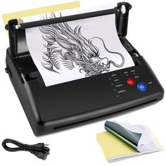 an inking machine with a dragon drawing on the screen next to some paper and scissors