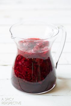 a pitcher filled with liquid sitting on top of a white wooden table covered in raspberries