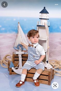 a little boy sitting on top of a wooden crate with a sailboat in front of him