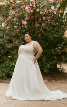 a woman in a wedding dress posing for a photo with pink flowers behind her on the ground