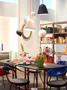 a dining room table with chairs and lamps hanging from it's ceiling, in front of bookshelves