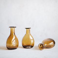 three glass vases sitting next to each other on a white surface with a bottle in the foreground