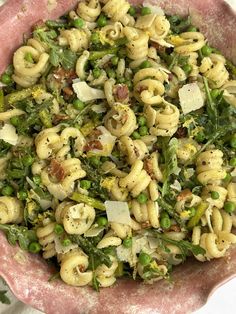 a pink bowl filled with pasta and vegetables