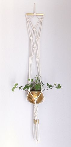 a white wall hanging with a plant in it and a gold bell attached to it