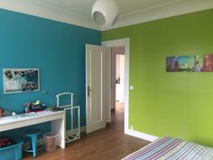 a bedroom with blue and green walls, wooden floors and a white desk in the corner