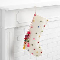 a white christmas stocking hanging from a mantel with pom - poms