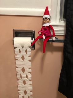 an elf is sitting on top of a toilet paper roll holder in front of a window