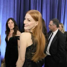 a woman with long red hair standing in front of blue curtained walls and wearing a black dress