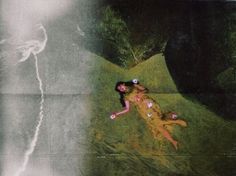 a woman laying on top of a lush green field next to a lightning bolt in the sky