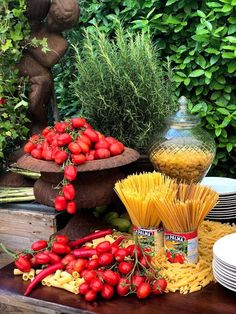 pasta, tomatoes and other vegetables on a table in front of some green bushes with a statue behind it