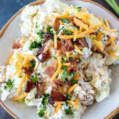 a white plate topped with potato salad covered in cheese and bacon next to green onions