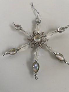 a snowflake made out of glass beads and silver chains on a white surface