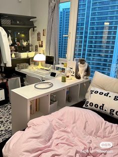 a cat sitting on top of a desk next to a bed in a room with large windows