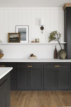 a kitchen with black cabinets and white counter tops is pictured in this image, there are pictures on the wall above the sink