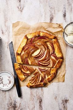 an apple tart with slices cut out on a piece of parchment paper next to a knife