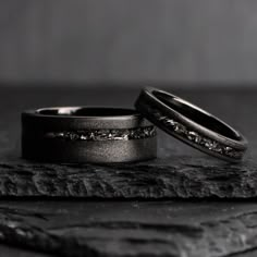 two wedding rings sitting on top of a wooden table next to each other with black diamonds in them