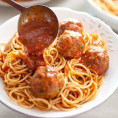 spaghetti with meatballs and sauce being stirred by a ladle on a white plate