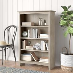 a room with a chair, table and bookshelf on the floor next to a potted plant