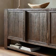 an old wooden cabinet with a bowl on top and books in the bottom drawer next to it