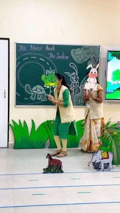 two people standing in front of a chalkboard with animals on it and one person holding a toy