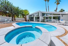 an outdoor swimming pool in front of a modern home with palm trees and patio furniture