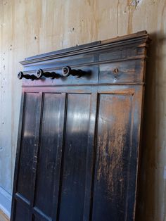 an old wooden cabinet with metal handles and knobs on the top, against a wall