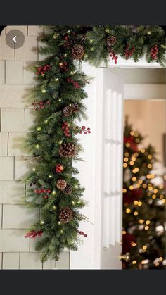 a christmas garland with pine cones and red berries hanging from the side of a fireplace