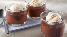 two glasses filled with dessert sitting on top of a blue tray next to spoons