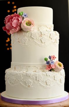 a three tiered white wedding cake with pink and purple flowers on the top layer