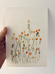 a hand holding up a piece of paper with flowers painted on it and gold flecks