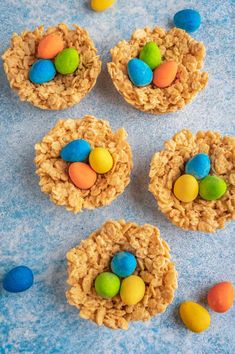 four cookies with candy eggs in them on a blue tablecloth next to candies