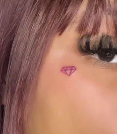 a woman's face with a small pink diamond tattoo on her left side eye