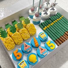 an assortment of decorated cookies and treats on a tray with pineapples in the background