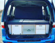 the back end of a blue van with an open trunk and two drawers on it