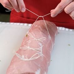 a person stringing up a piece of meat on a white board with twine