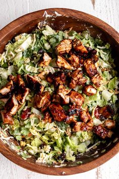 a salad with chicken and lettuce in a wooden bowl on a white surface