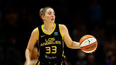 a woman holding a basketball in her right hand and looking up at the ball she is about to shoot