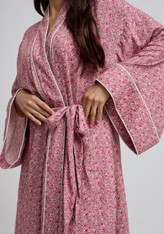 The charming Corina robe is cut from our inimitable cotton and adorned with an interesting pink Ditsy floral print. This oversized kimono-inspired robe boasts fluted sleeves and a detachable belt, creating a flattering silhouette. Contrast piping on the cuff and neck, complete this effortlessly feminine piece.  Cool machine wash only. Wash inside out and with similar colours 100% Cotton Sourced India  Cool machine wash only. Wash inside out and with similar colours Feminine Floral Print Robe For Loungewear, Pink Cotton Sleep Robe, Red Floral Print Sleepwear For Spring, Spring Cotton Robe With Floral Print, Cotton Floral Print Robe For Daywear, Pink Floral Print Home Robe, Pink Floral Print Robe For Home, Pink Feminine Robe For Sleepover, Feminine Pink Robe For Sleepover