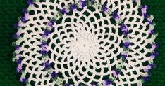 a crocheted doily with purple and white flowers in the center on a green background