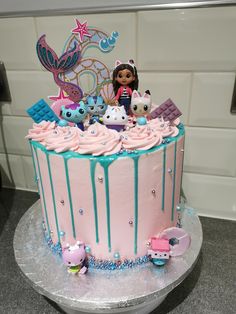 a pink and blue cake with littlest pet shop figures on top, sitting on a table