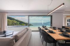 a dining room table with black plates and place settings in front of a large window overlooking the ocean