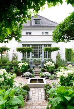 an outdoor garden with white flowers and greenery in front of a large house, surrounded by trees