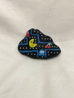 a black rock with blue and yellow designs on it sitting on a white cloth covered surface